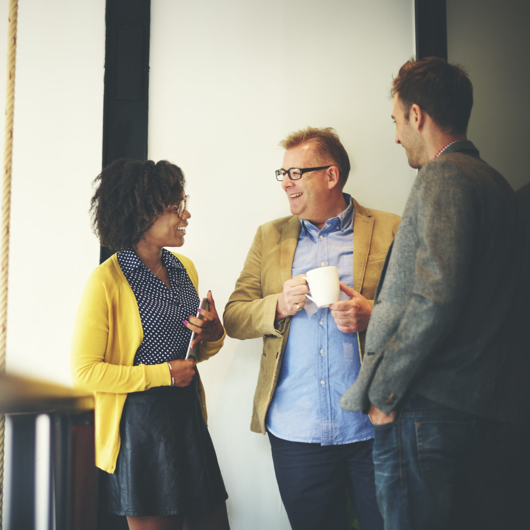 Three people in office wear standing and talking with smiles