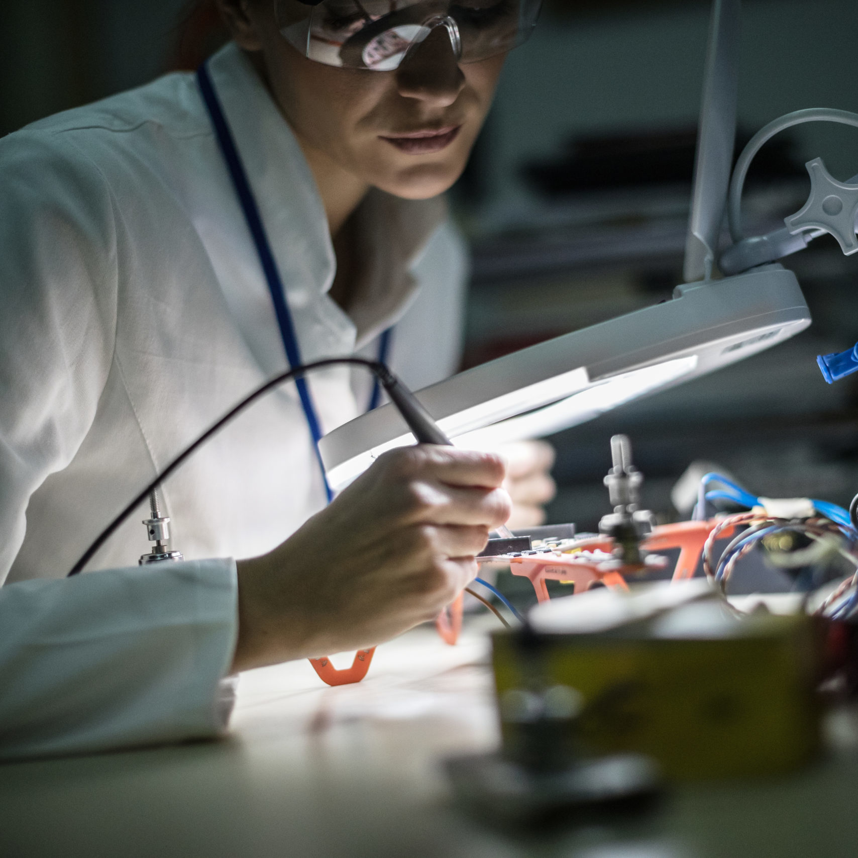 Mid adult female electrician working on electrical equipment, using magnifying glass.